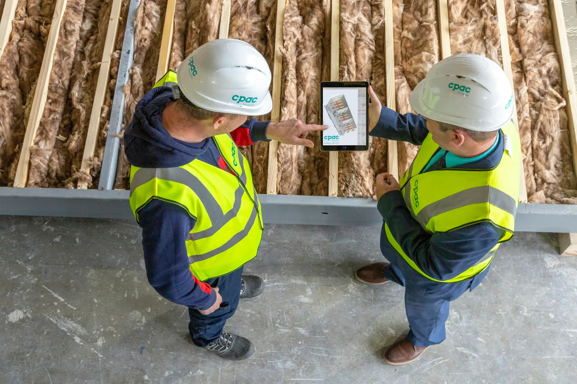 Two workers reviewing a plan on a tablet inside a partially built room