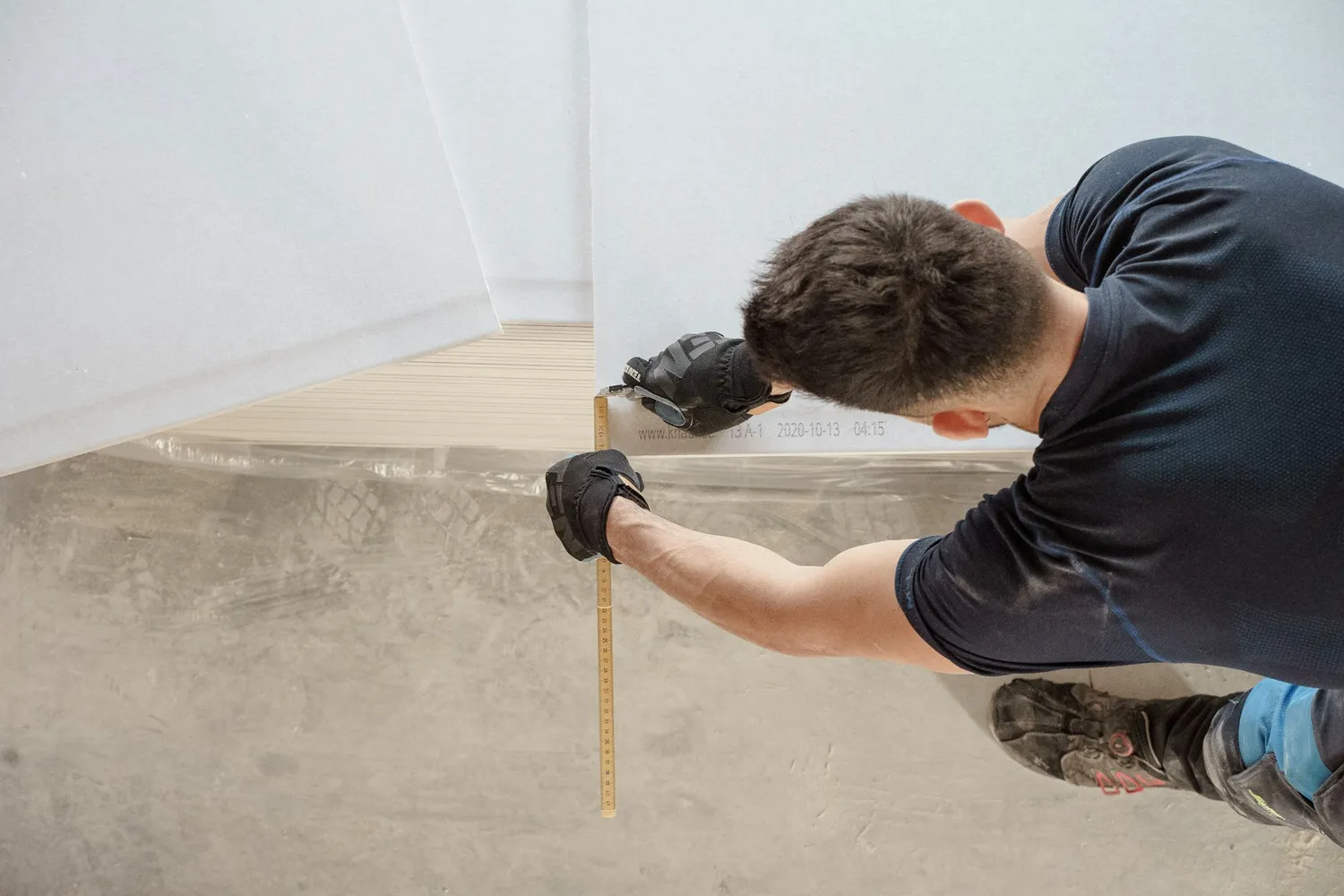 An installer measuring over a vapour barrier on a concrete slab